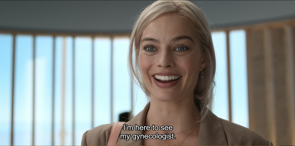 A smiling Barbie (played by Margot Robbie) arriving to her gynecologist appointment dressed in a beige blazer with her blond hair tied back.
