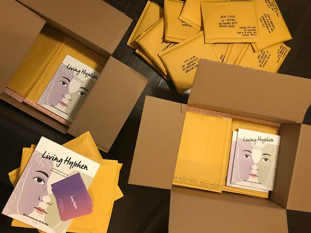 Aerial view of two boxes filled with yellow envelopes and Living Hyphen magazines. More magazines and envelopes are scattered