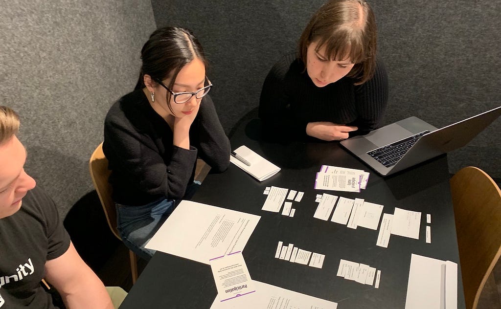 Three people gathered around a table looking at different elements of Shopify’s products page.