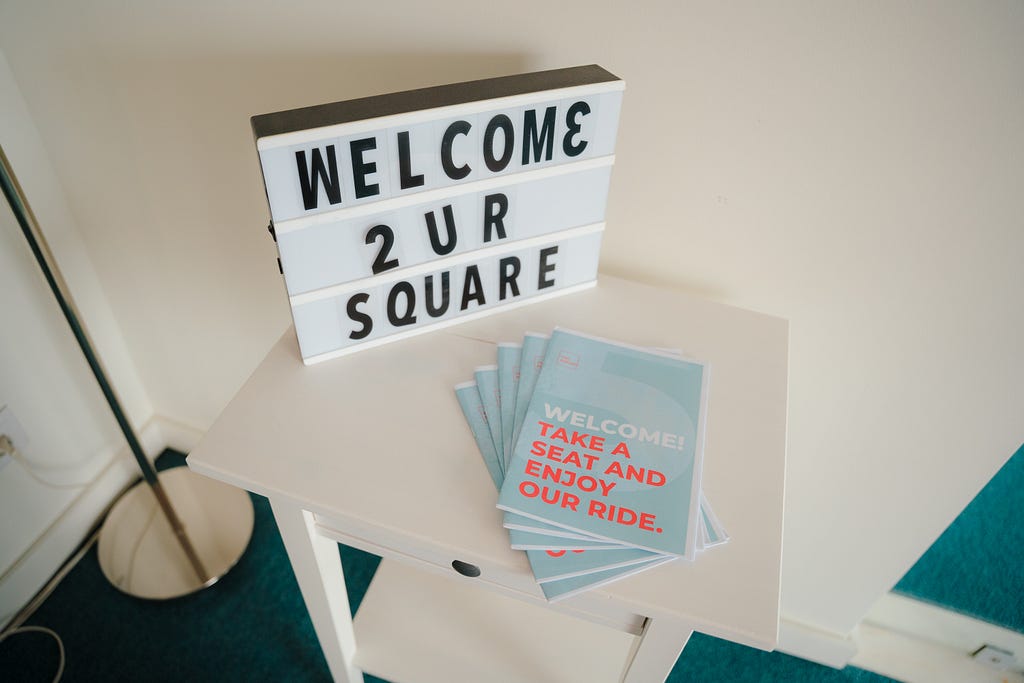 a side table with some brochures on top and a sign saying welcome to the square