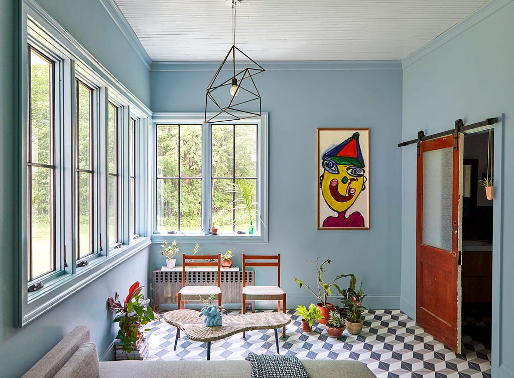 A spacious sunroom with windows on two sides plus a quirky childlike clown painting.