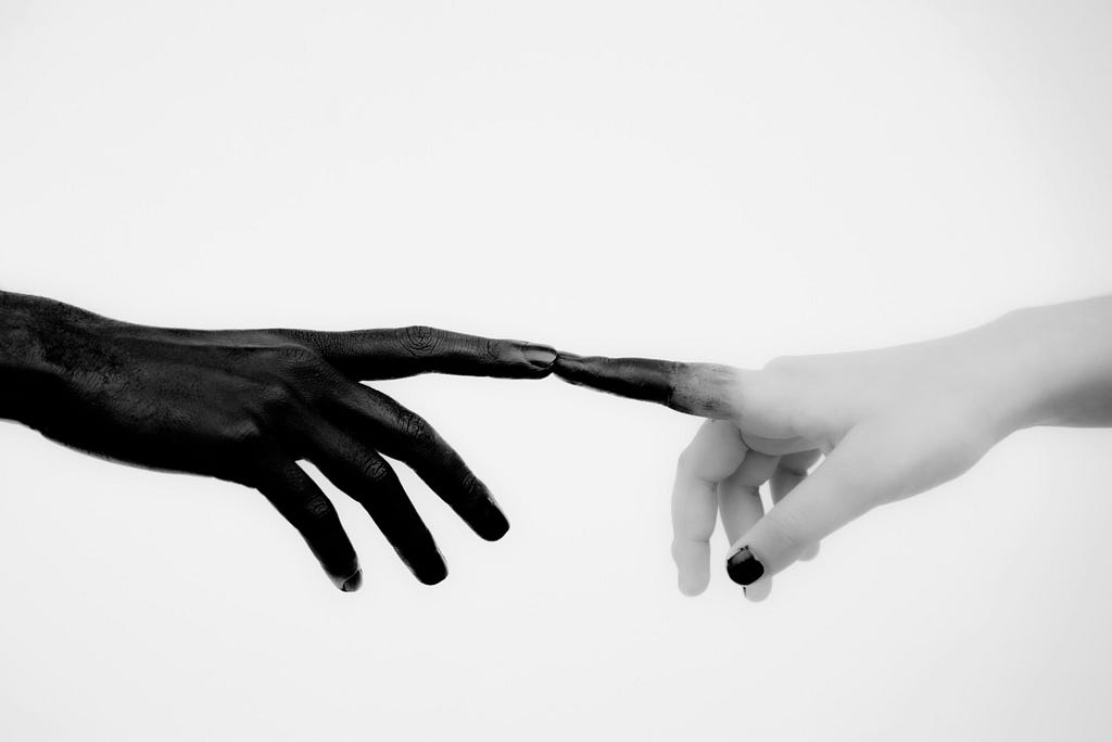 The tip of a black hand in the left touching the tip of a white hand in the right with some of the black bleeding through