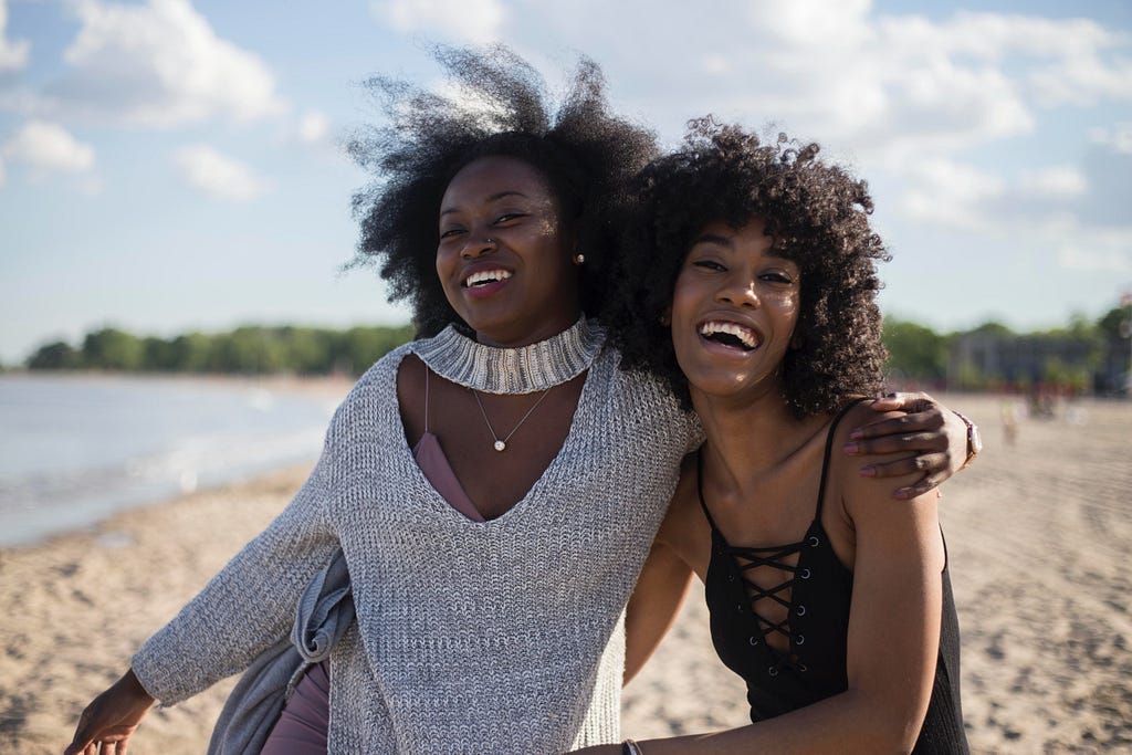 two black women with beautiful curly hair smiling on a beach