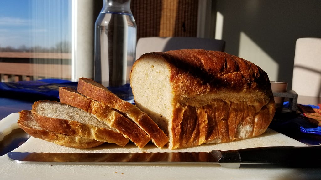 A sunlit loaf of bread with four slices exposing the deliciously open crumb