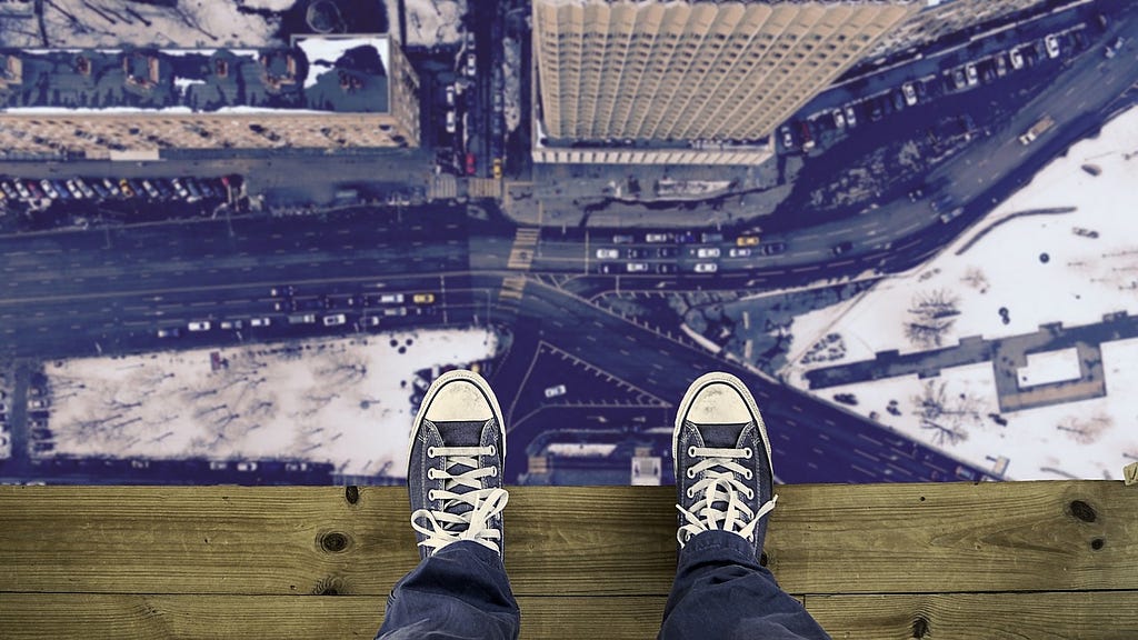 a persons shoes at the edge of a balcony overseeing the city. this is supposed to represent courage. courage to look down at what is scary. what is real.