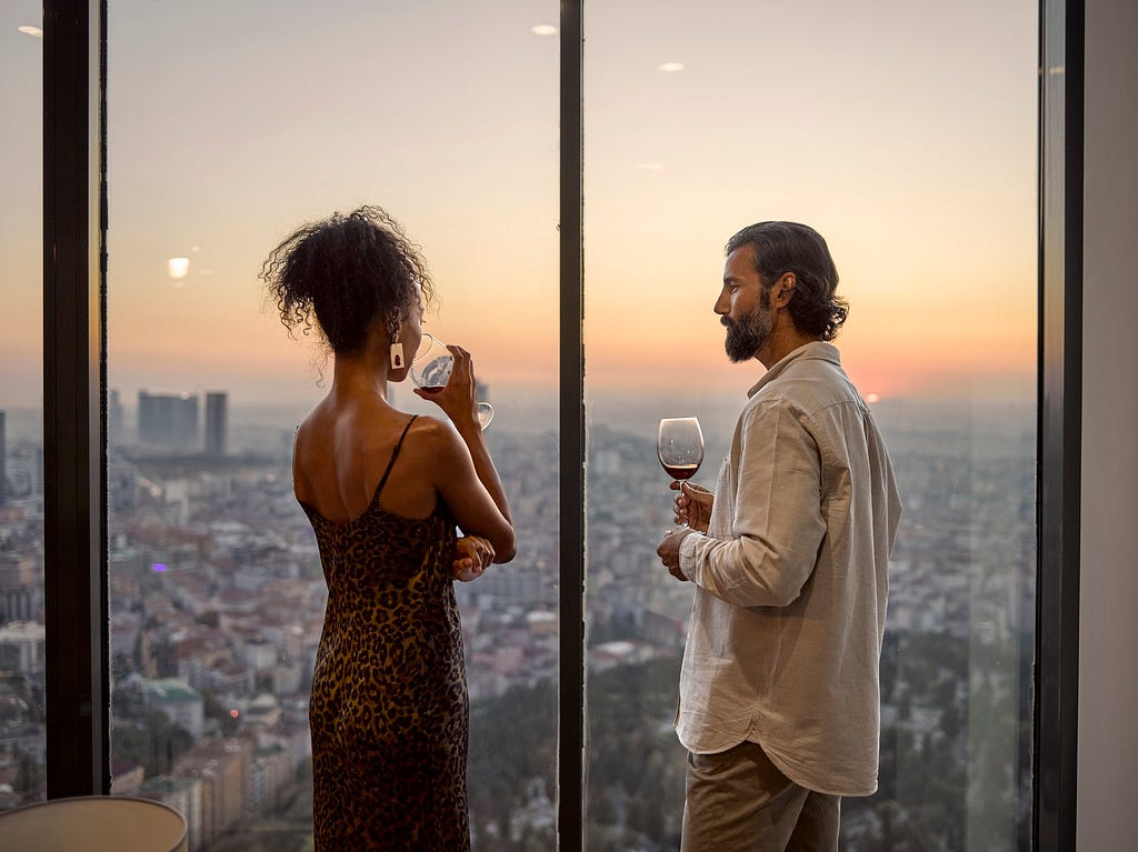 Attractive couple enjoying red wine while looking out over city at sunset