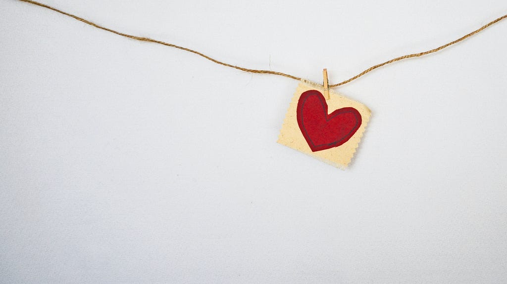 red heart on postcard sized piece of paper hanging from string