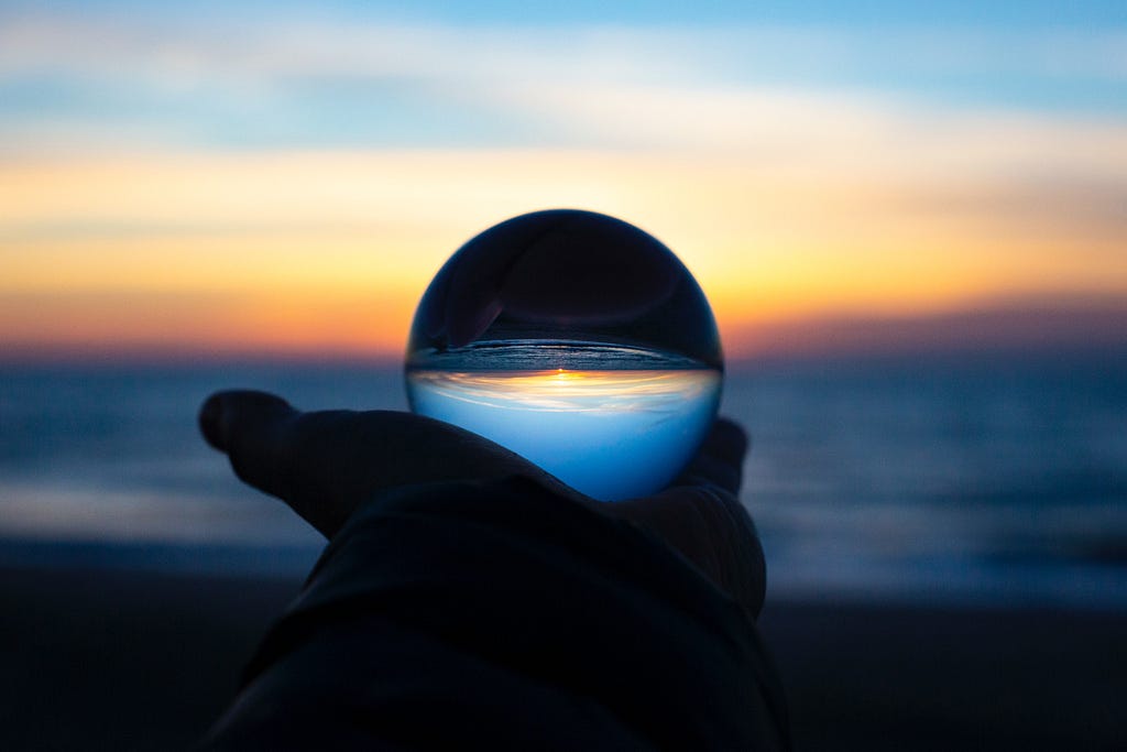 A crystal ball held up against a dark ocean sunset