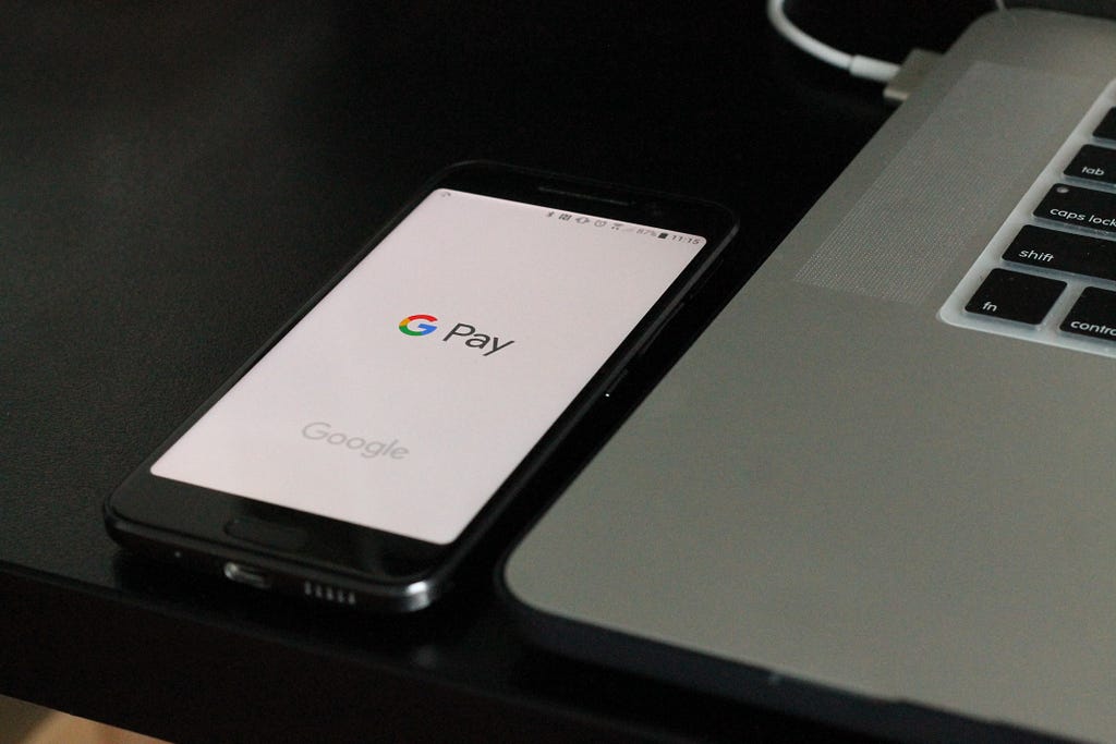 Picture of a mobile phone with the Google Pay app open next to a Mac.