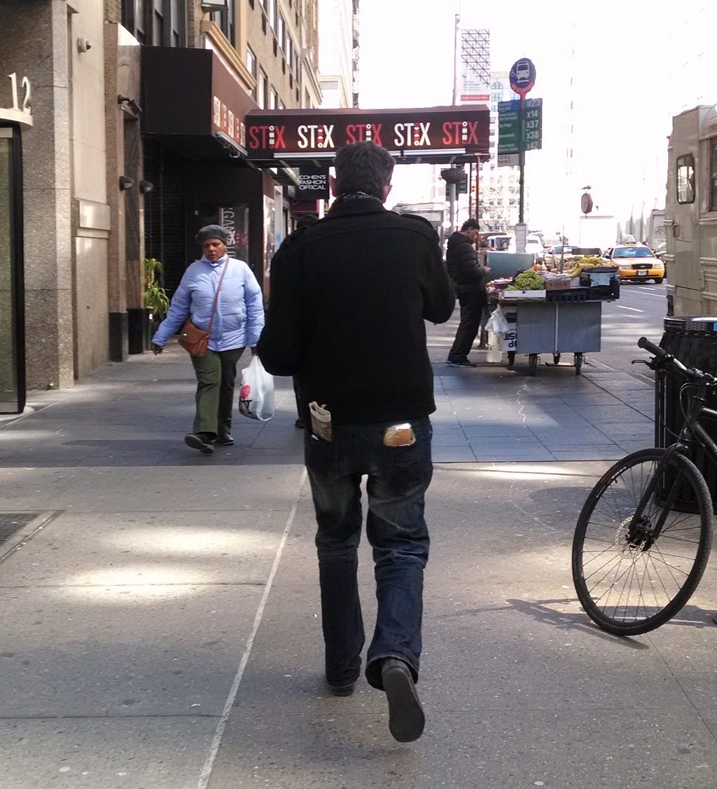 Man walking down a city street with a sandwich in back pocket