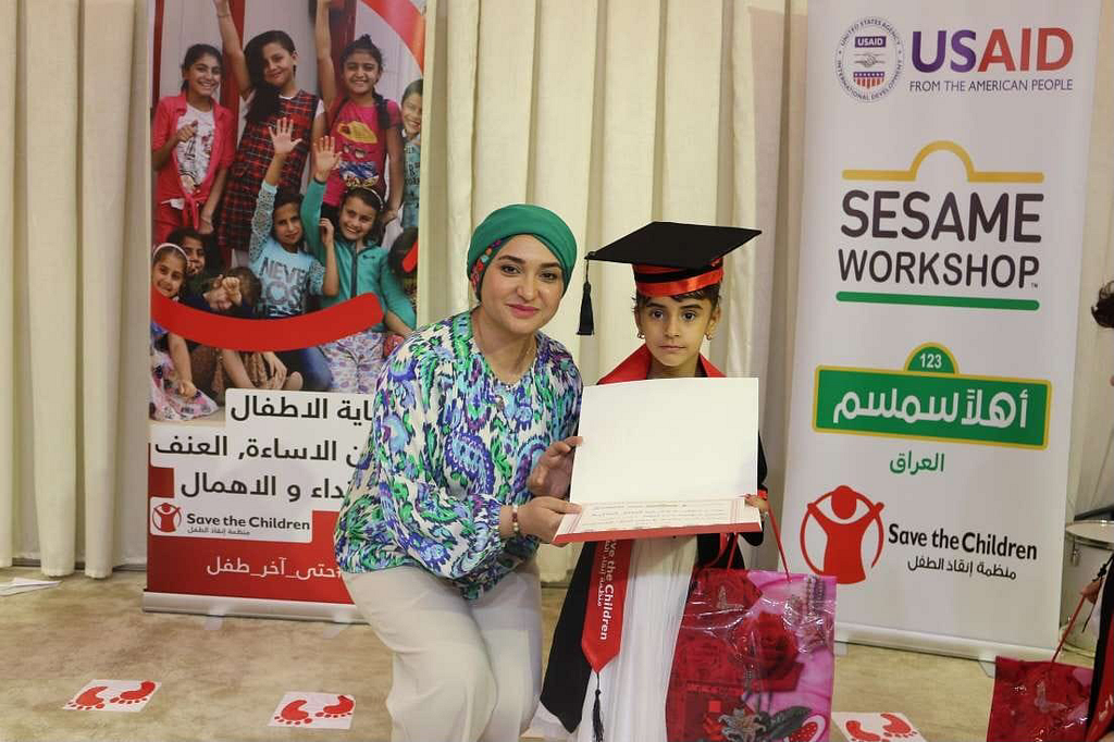 A woman takes a photo with a little girl holding her certificate during a graduation ceremony.