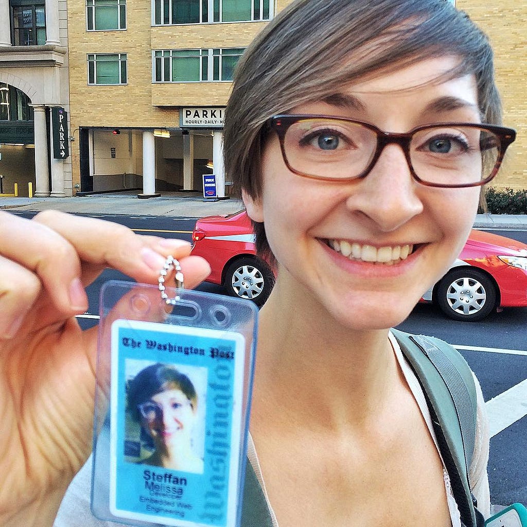 The author on her first day working as a software engineer at The Washington Post. She is holding up her blue employee badge, wearing a huge smile.