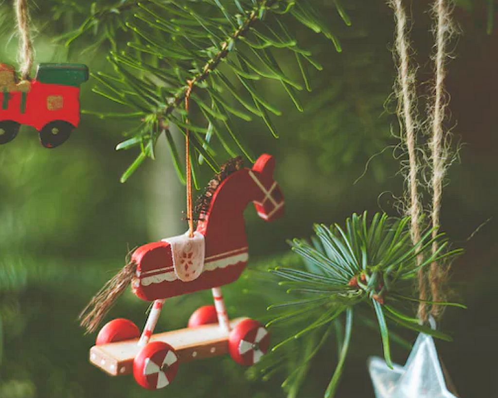 A red wooden horse decoration hangs on a Christmas tree.