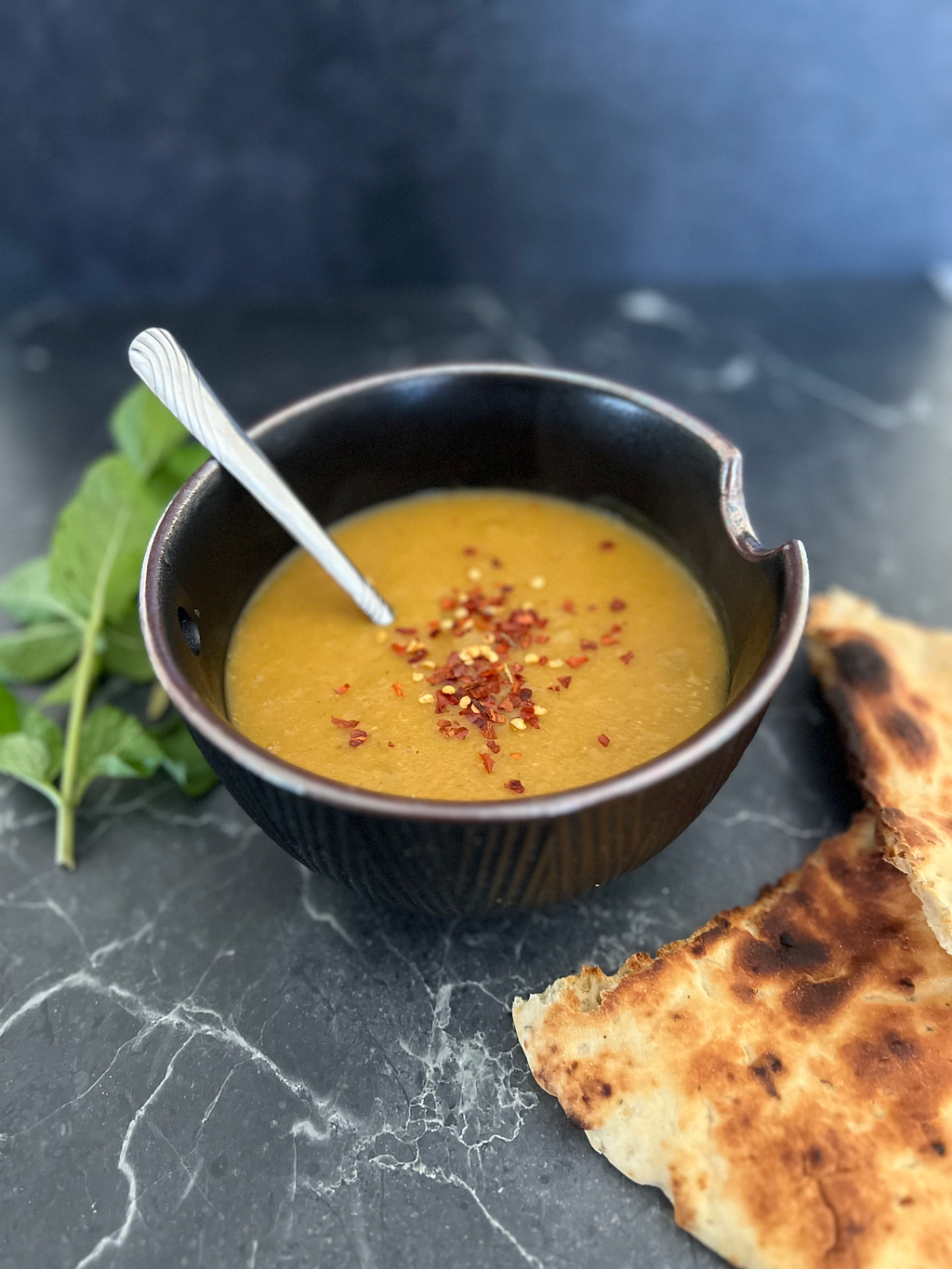 Lentil soup on a marble countertop with toasted naan and mint