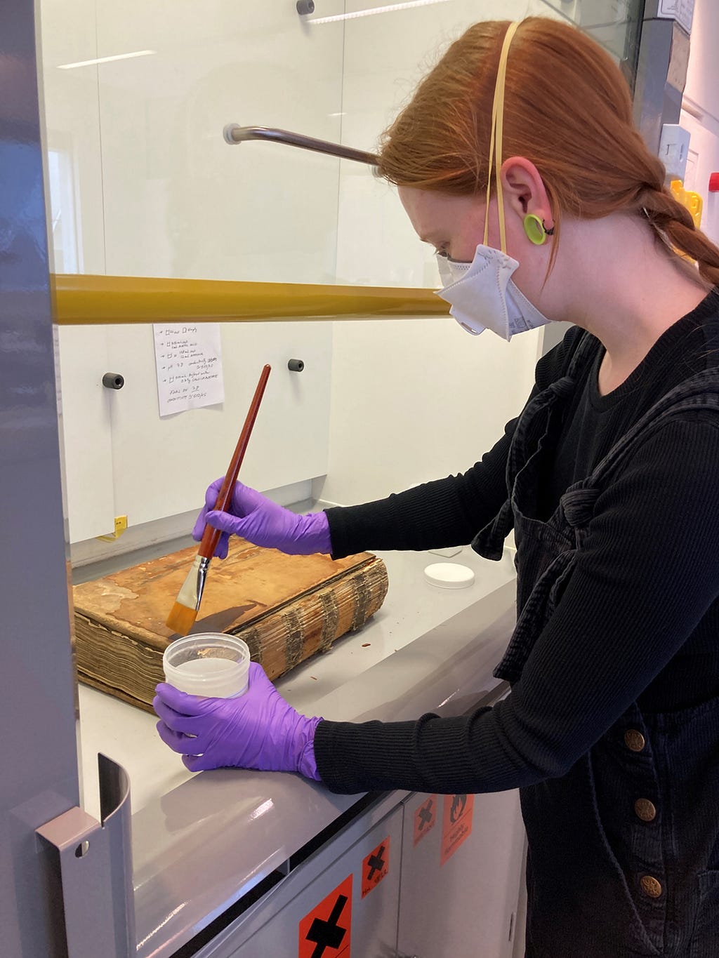 Sabeth brushing Klucel-G onto a leather-bound book [Image credit: Iris Matthews]