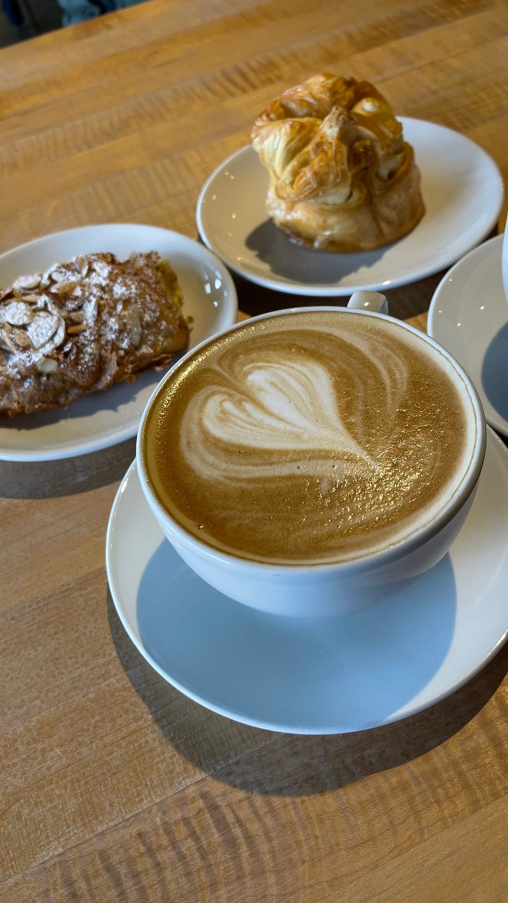 A latte with heart-shaped foam art in a white cup and pastries arranged behind it