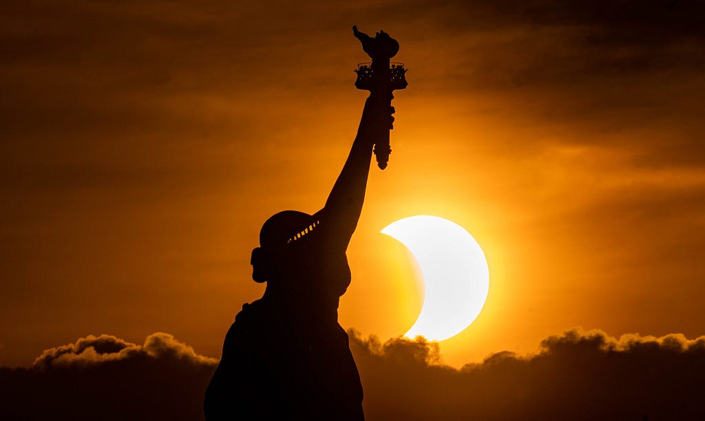Silhouette of Statue of Liberty with eclipse on the horizon