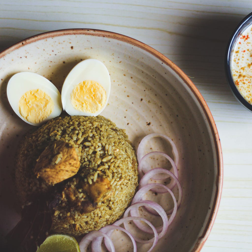 Vertical view of Biryani, served with onions, boiled eggs and raita
