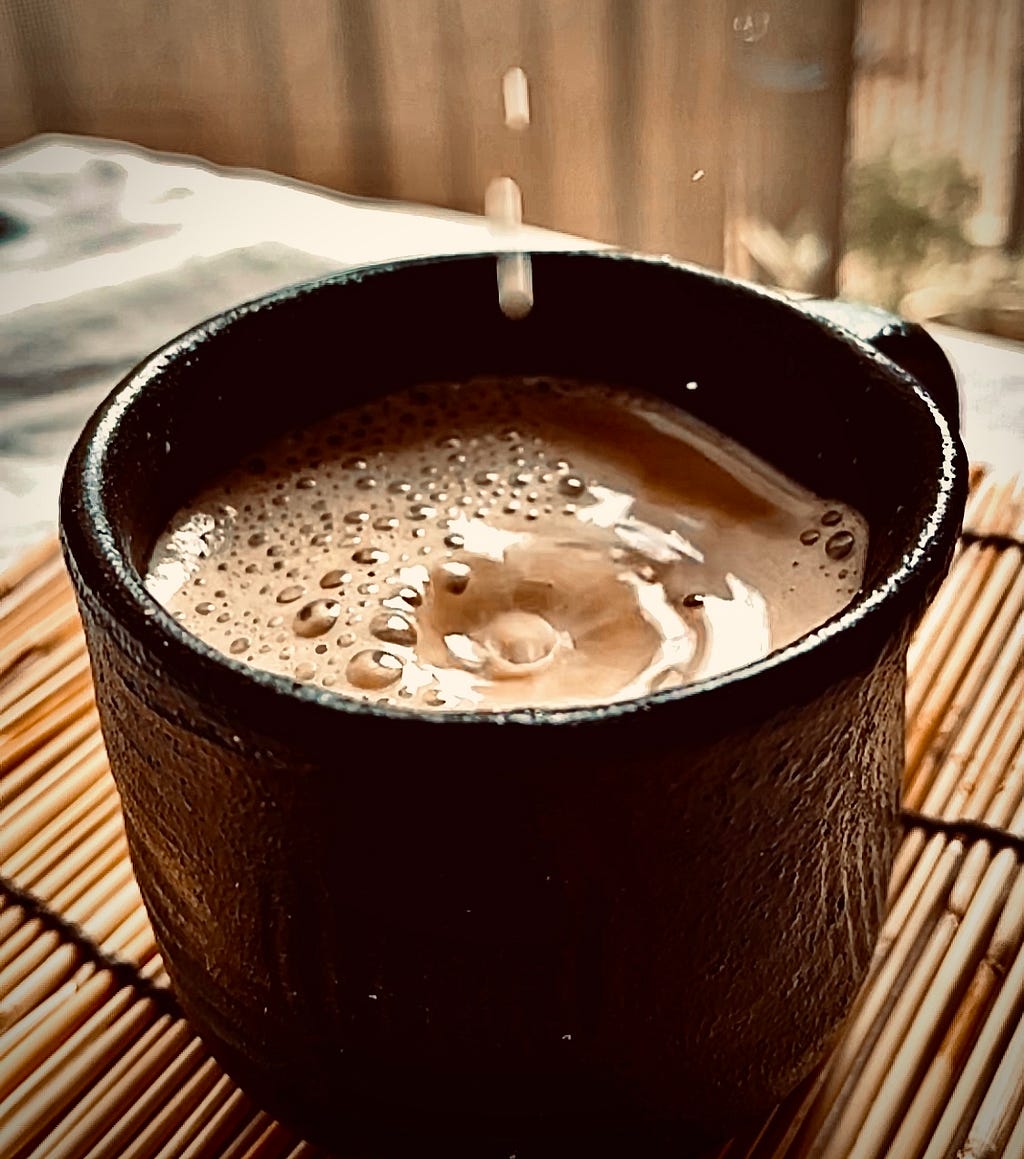 A dark brown textured ceramic mug with coffee and milk dropping on to its foamy surface