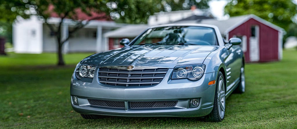 Panoramic photograph of a (likely) 2013 Chrysler Crossfire with a red polebarn in the background.
