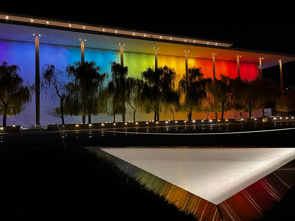 Night time rainbow lights illuminate the pillars along the rear of the Kennedy Center which faces the Potomac River