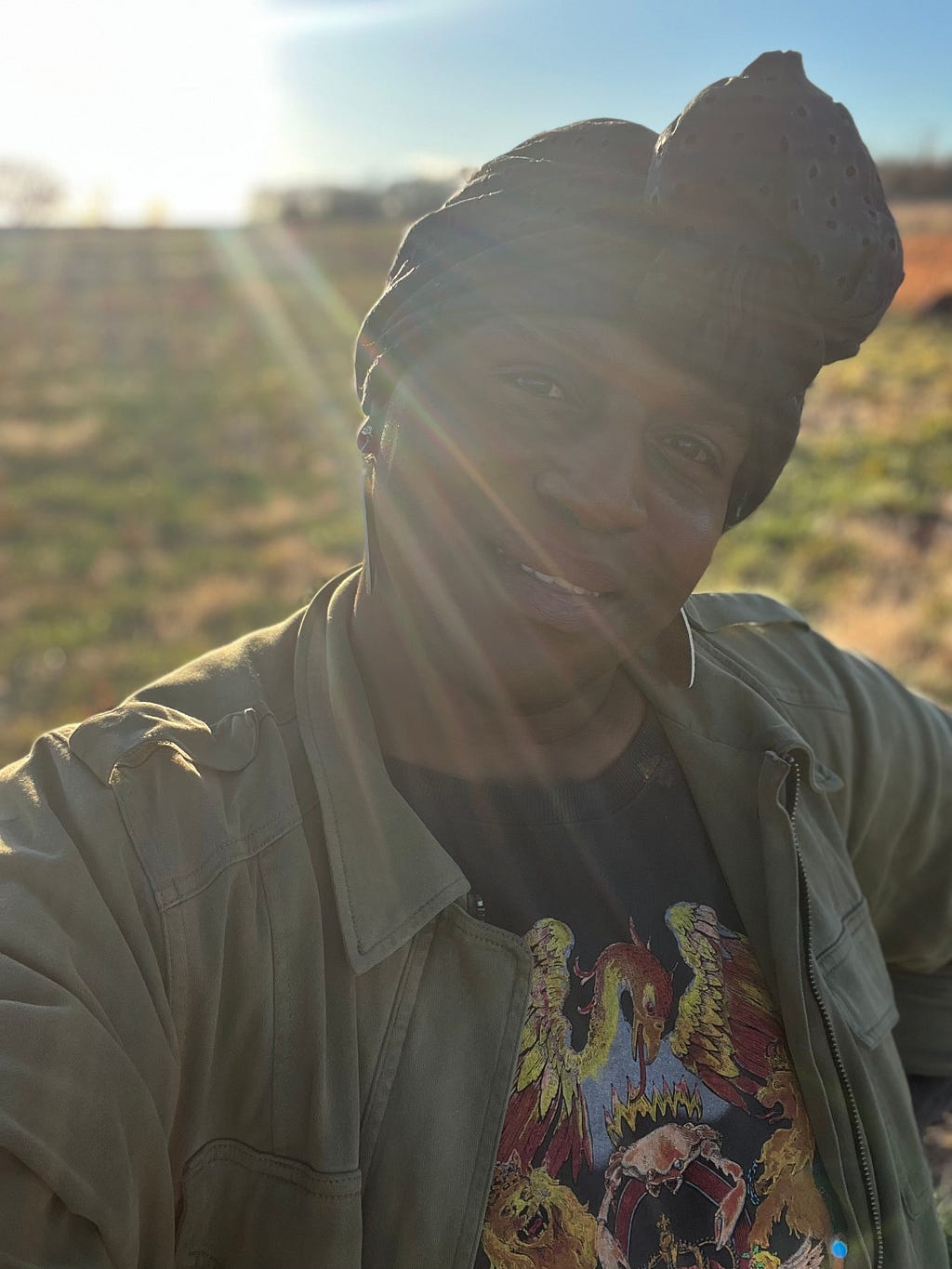 Black trans human standing in a field with the sun on their back. the human is looking directly at the reader. the human is saying- you’re going to have to deal with me as I am.