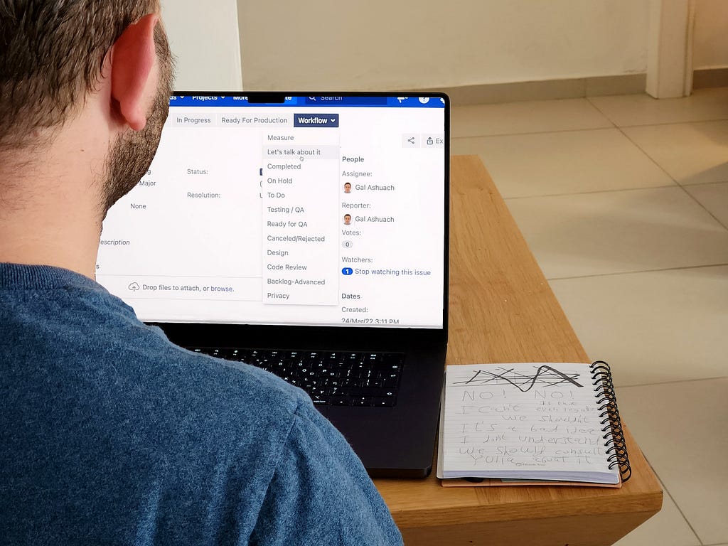 An image of a software engineer working on his laptop, switching the status of a new task he was given to “Let’s talk about it”.