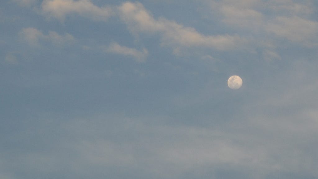 The moon somewhat hiding behind thin clouds, but still visible enough to witness her beauty.