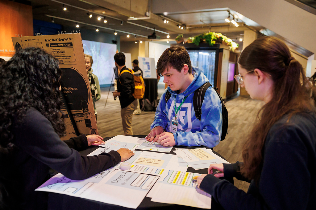 Three students look at a papers on a table.