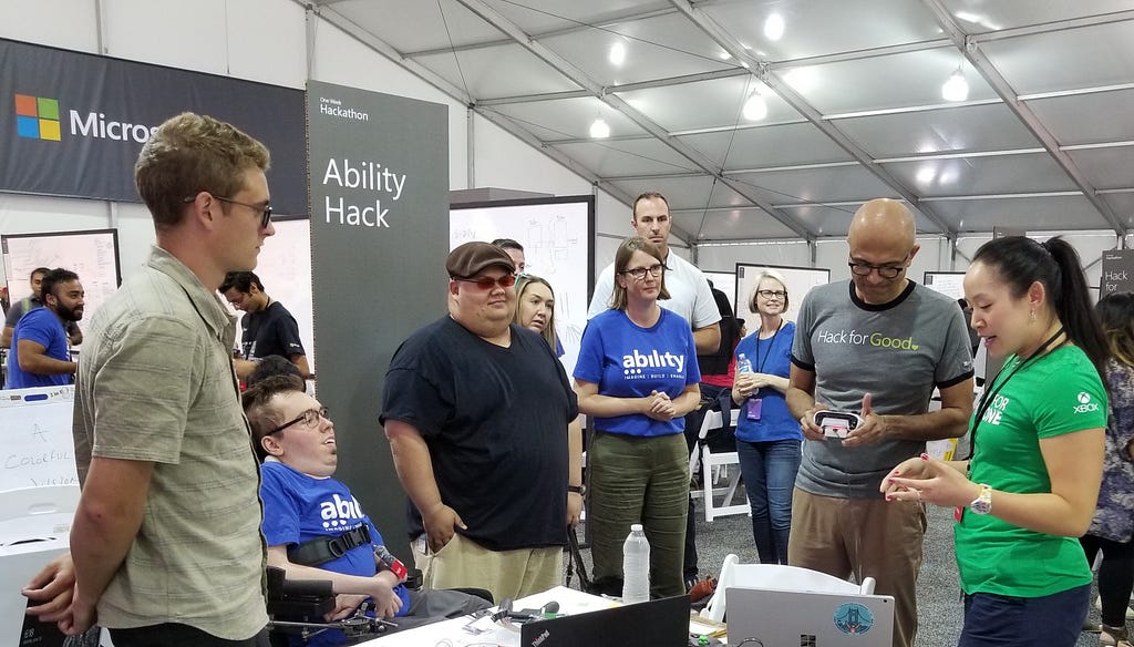 A crowd has formed around the Hackathon team as they demo their project for CEO Satya Nadella and CAO Jenny Lay-Flurrie.