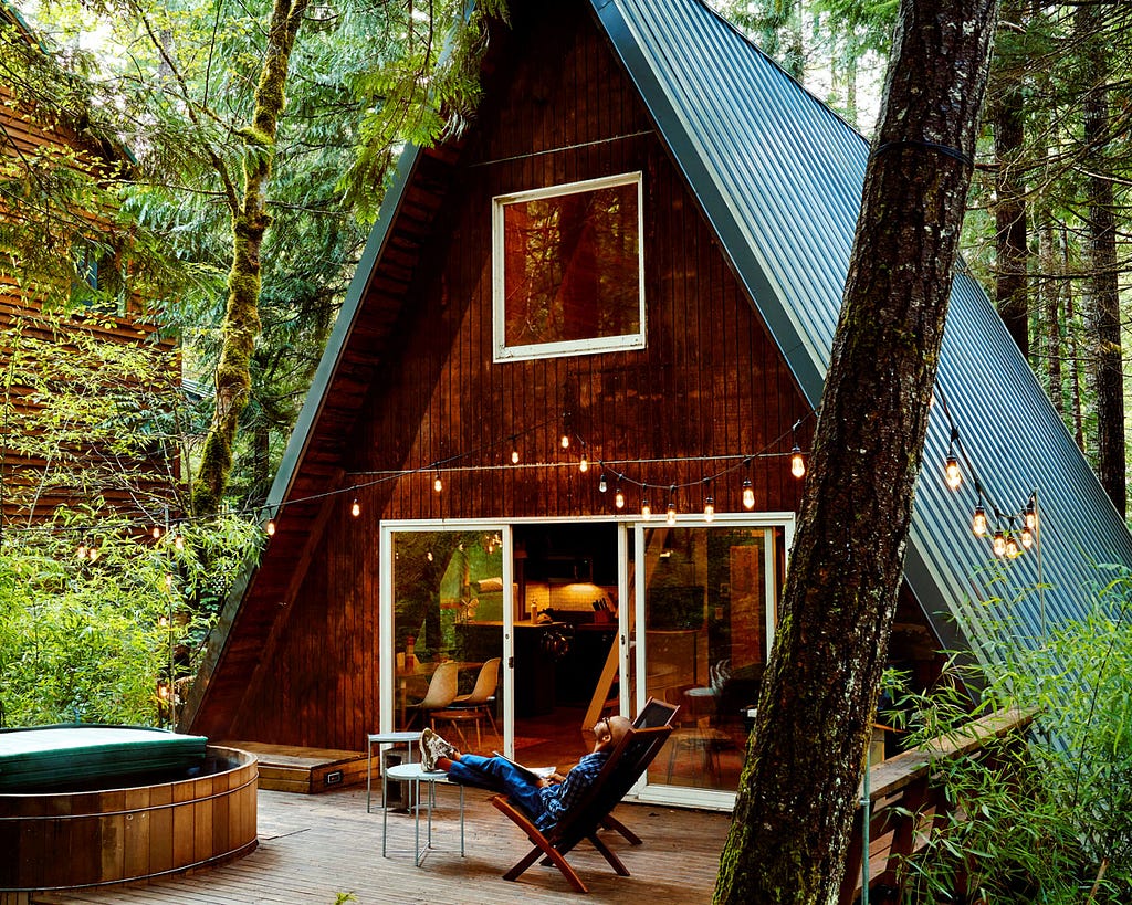 A man sits outside an A-frame house deep in the woods in Washington State.