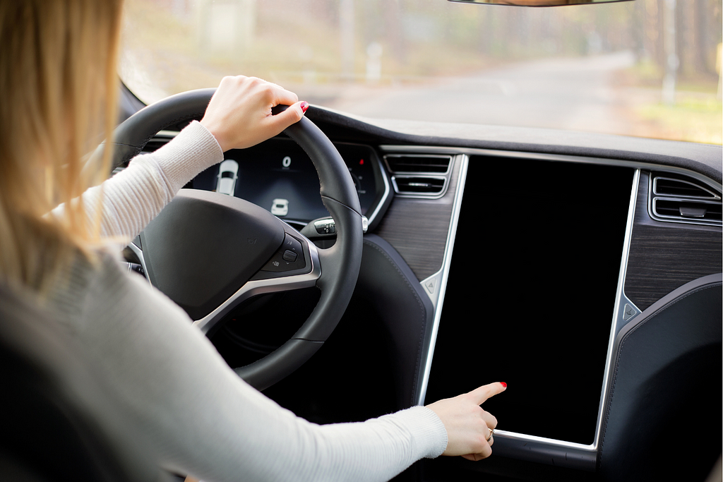 A woman drives a Tesla Model 3 with a large touchscreen center console. Known as an example of modern technology in cars, Teslas require several different onboard computers as well as servers to remotely store and process data.