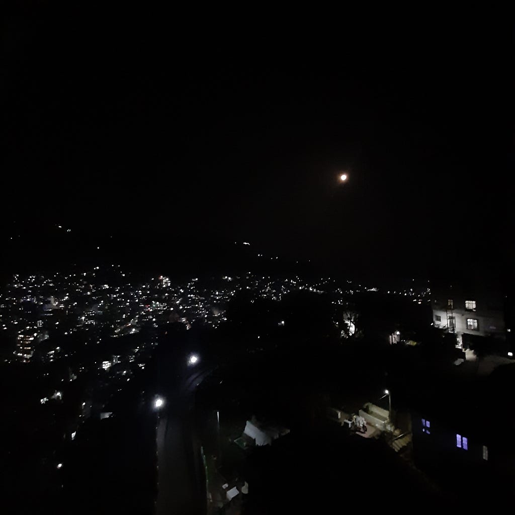 Night city lights in mountains with the moon