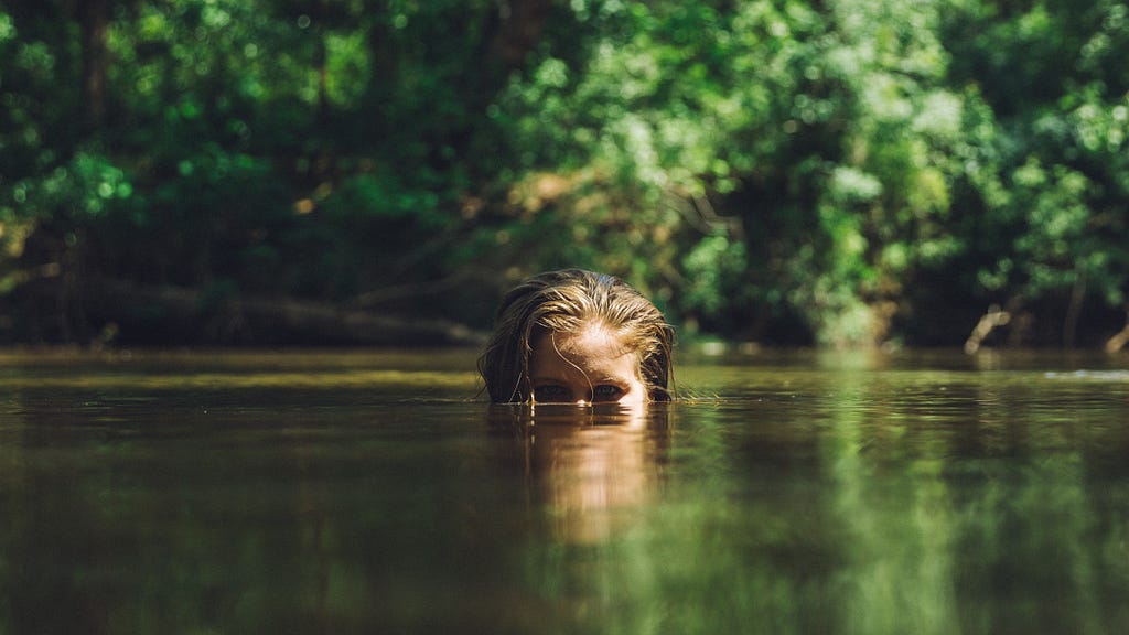 little girl in a river with only eyes and top of head visible above the water