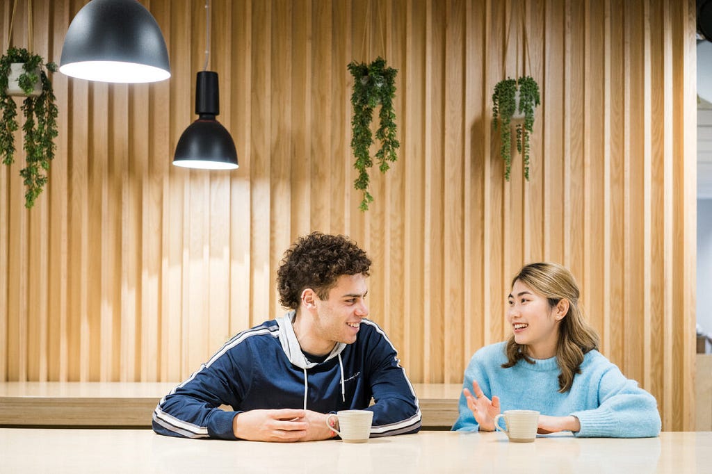 two students sat chatting to each other with a cup of coffee.