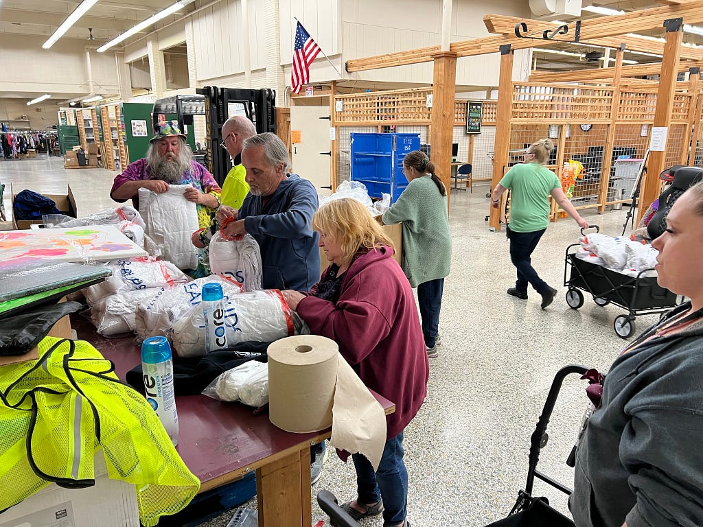 Five of The Moore Wright Group staff members work together to place blankets in bags inside the organization’s warehouse location. Two other staff members are working in the background.