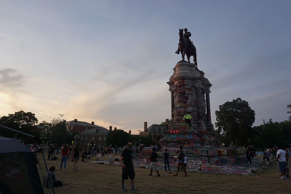 People walk around a statue of Robert E Lee at sunset