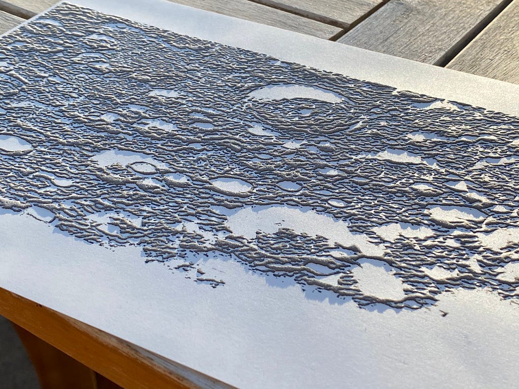 A tactile map of a heavily-cratered landscape where topographic highs are raised and topographic lows are smooth.