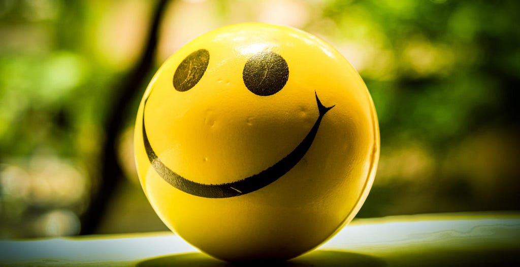 A small yellow sphere with a happy face painted on it sits in the sunlight
