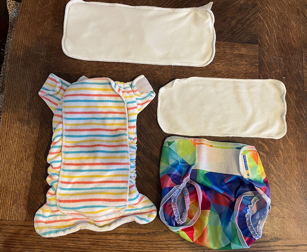 A stripey cloth nappy, with a white booster and white liner, and a multicoloured wrap with velcro