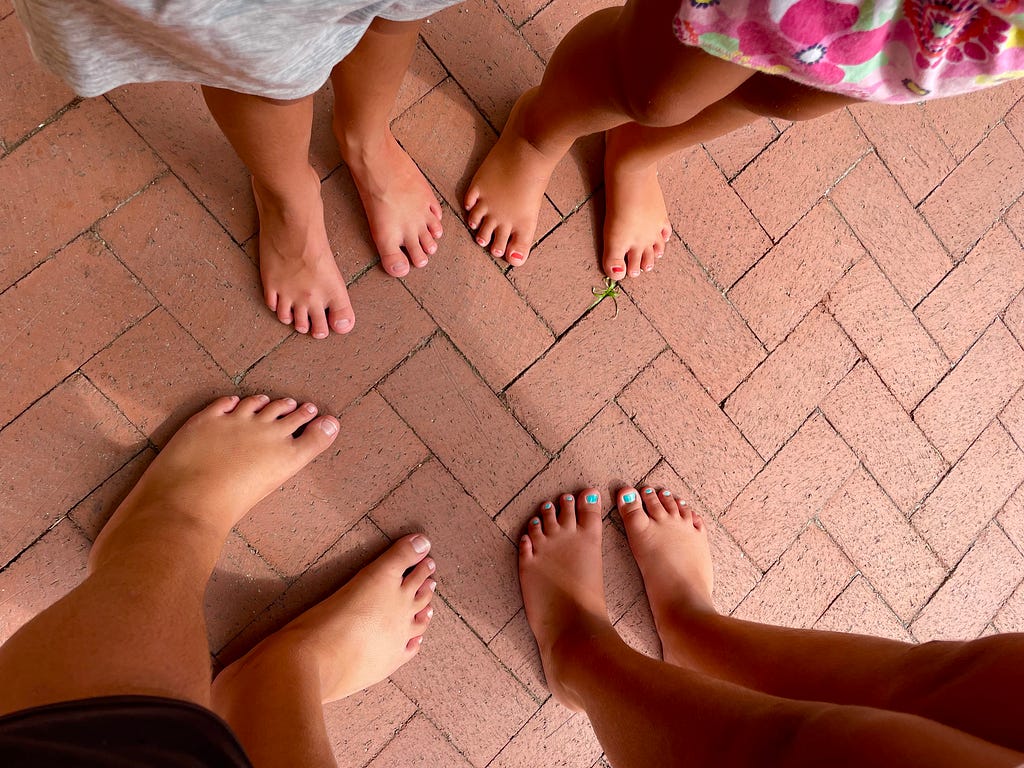 The barefoot feet of four children standing together on a brick patio