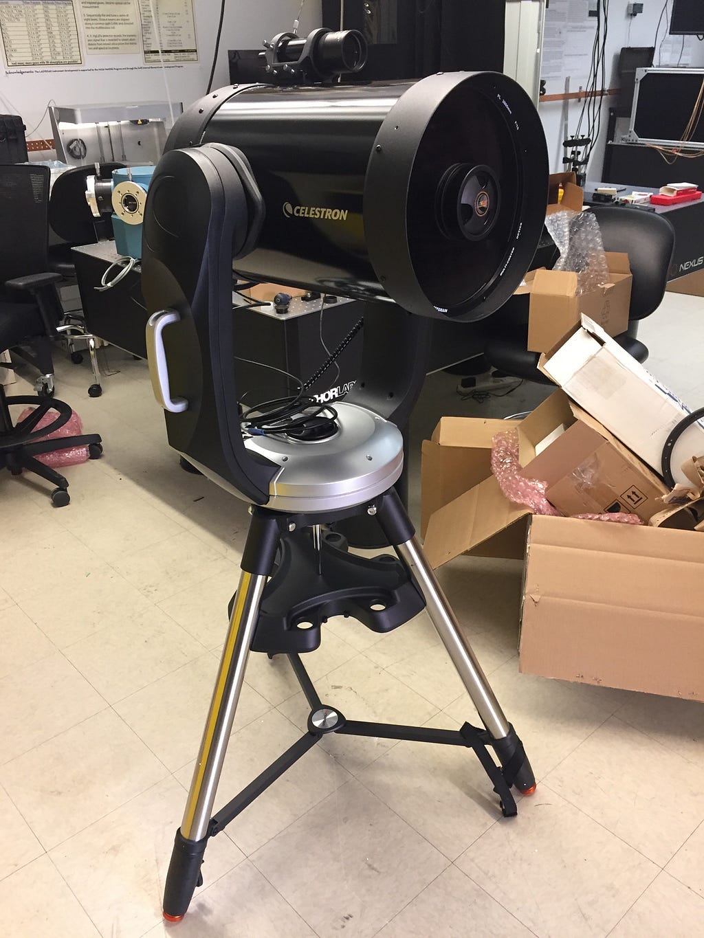 A portable celestron telescope set up indoors in a laboratory. Discarded boxes and bubble wrap are in the background.