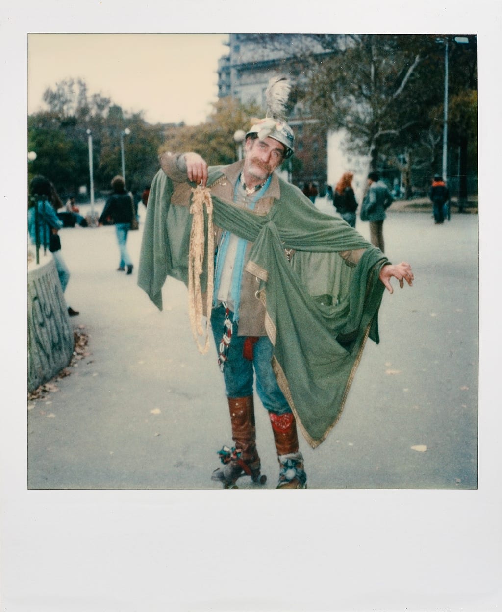 In a park, a man wearing rollerskates and an elaborate shawl, plus a helmet, poses for the camera.