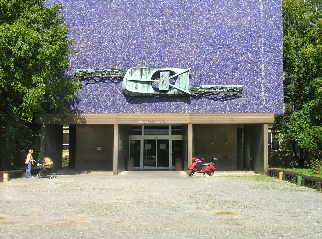 Front face of a concrete building, purple in colour, with a stylized transistor sculpture above the entrance.