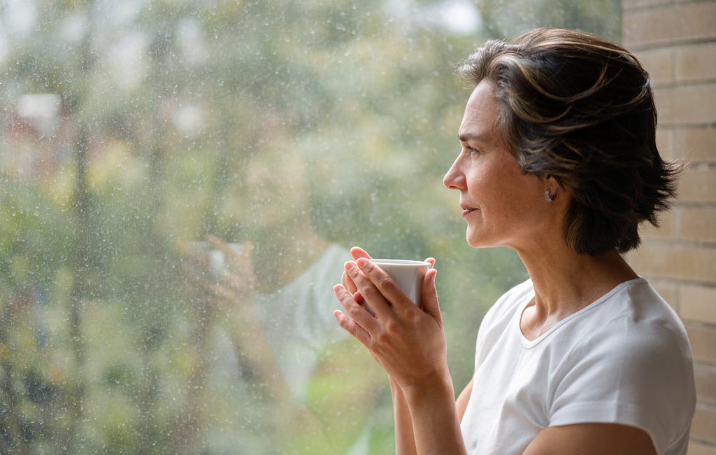 Pensive woman drinking from cup looking out a window