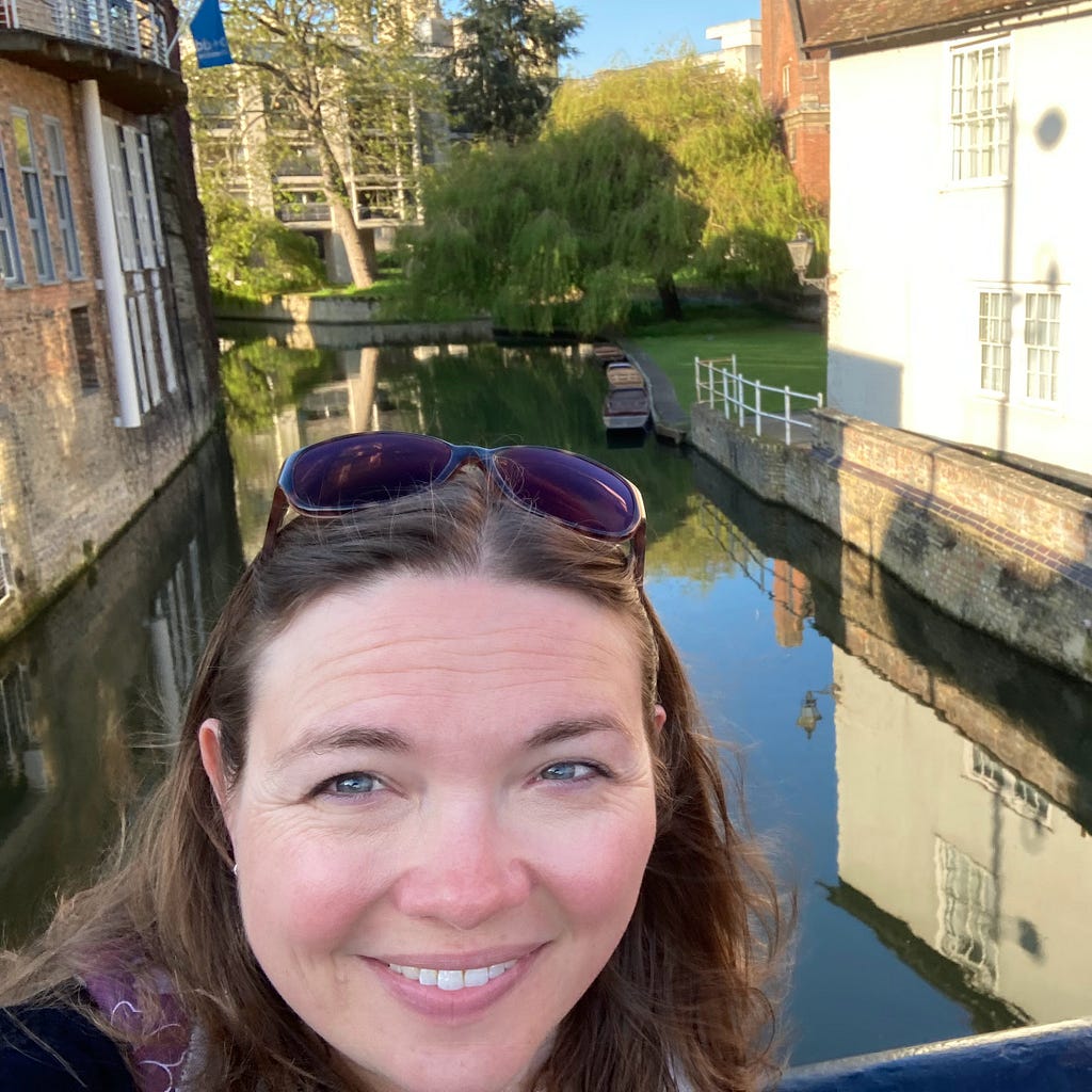 Photograph of me with the River Cam behind me and some punts, Willow trees, neo-gothic architecture