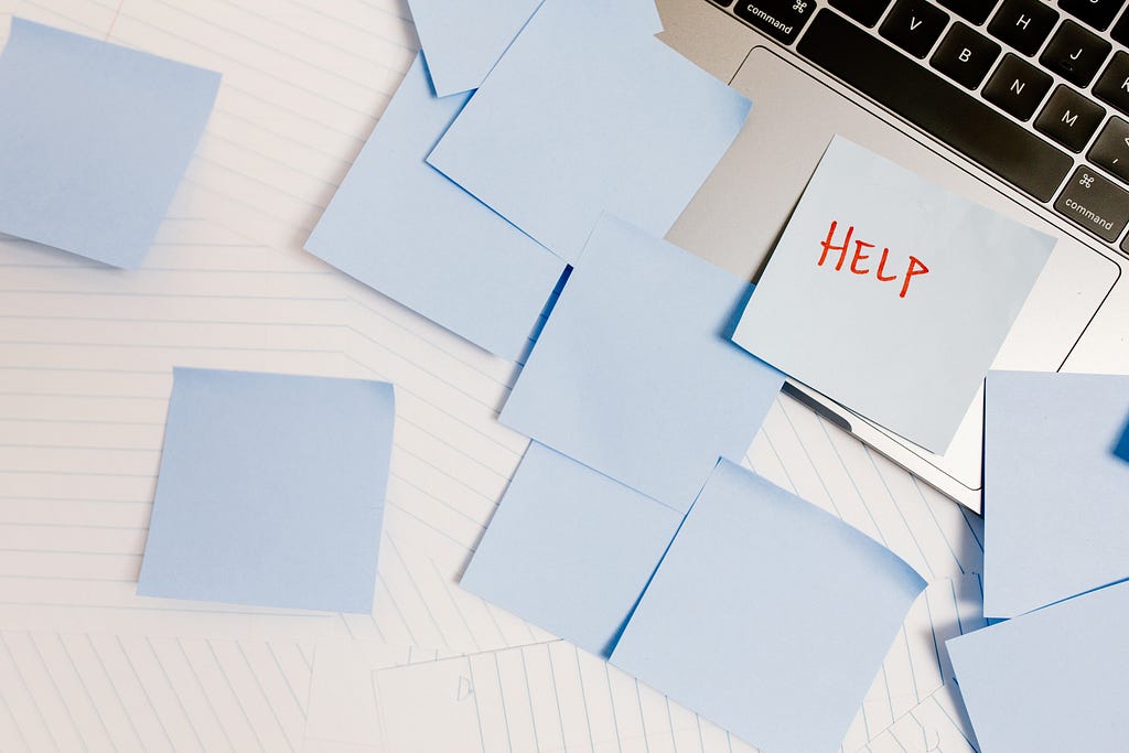 Blue sticky notes adhered to a laptop, one with the word ‘help’ written on it in red ink.