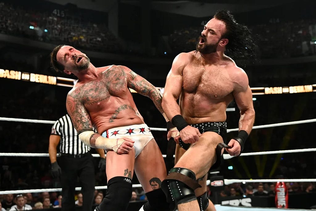 Two sweaty and tatooed professional wrestlers engage in a fake fist fight in a professional wrestling match.