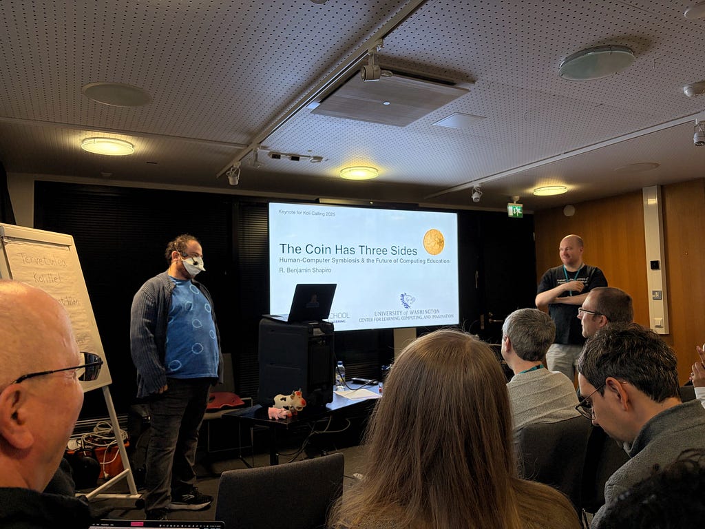 Ben standing a the front of the room in front of a slide that says “The Coin has Three Sides”.