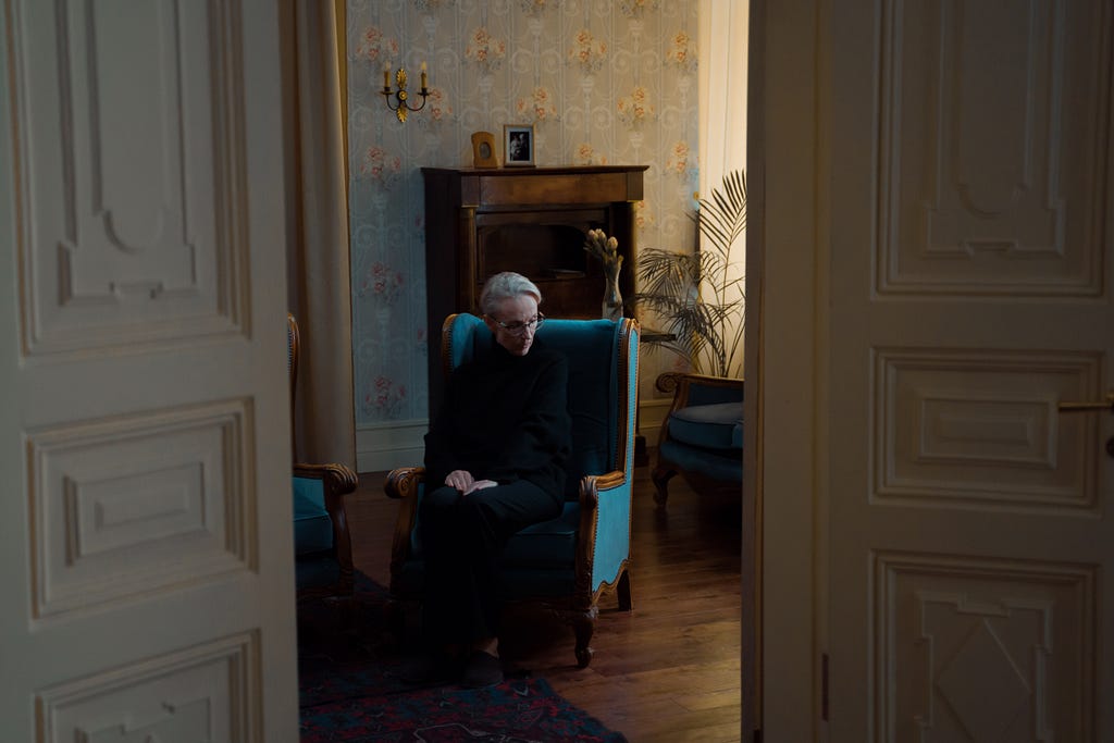 An old lady sitting in a large blue armchair, looking lonely.